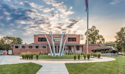 Photo of the Nebraska National Guard Museum: a low brick building behind a sculpture of four military jets soaring upwards. A flagpole with an American flag and a tank are also in front of the building.