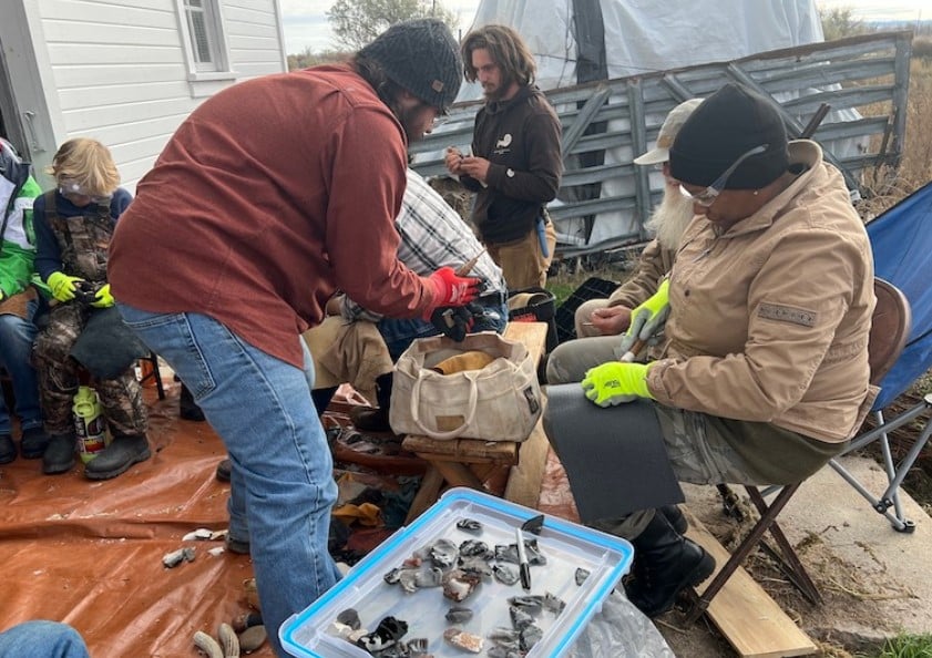 Class participants wearing safety gear sit in a circle and use tools to shape stones.