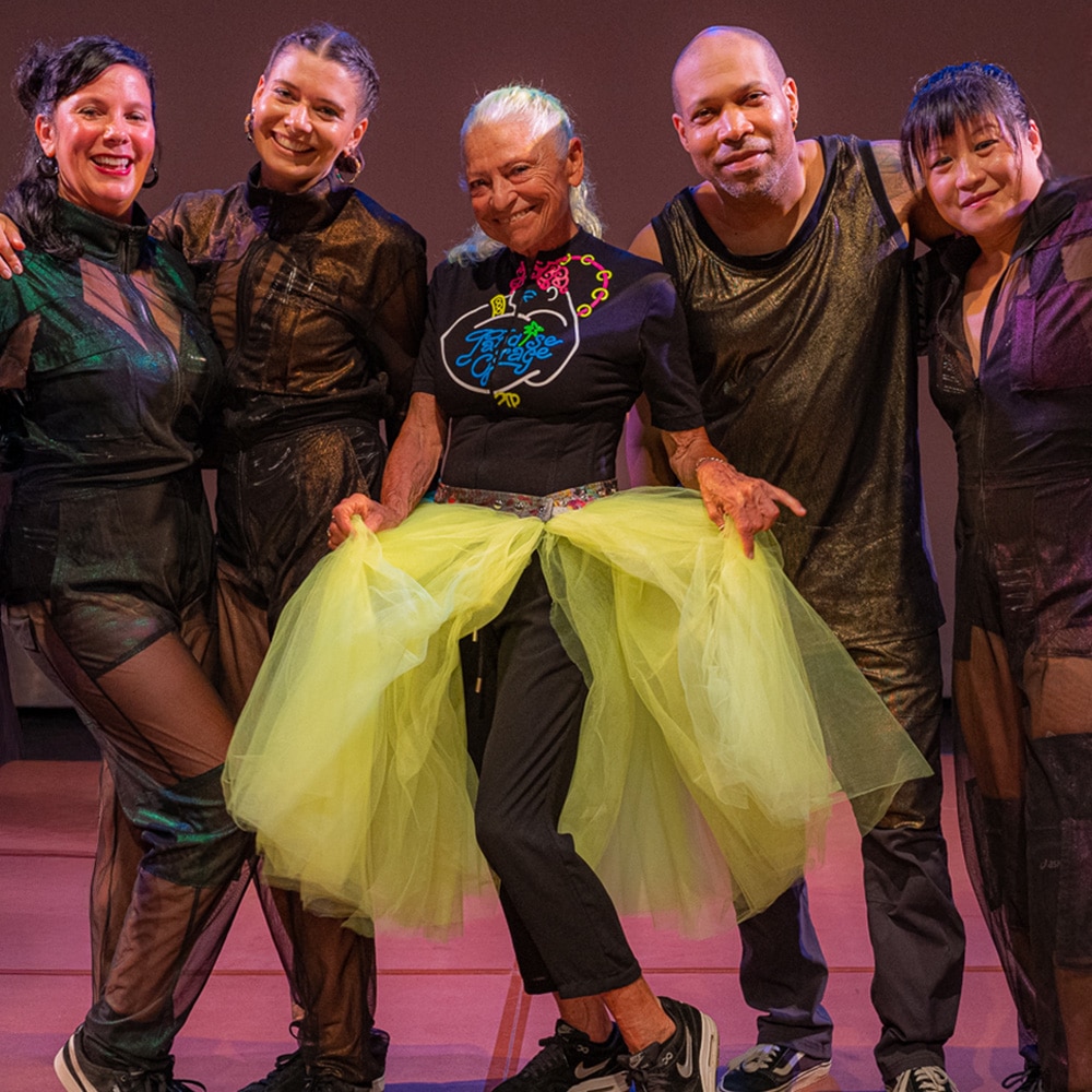 Five people in dance attire. The person in the middle is holding out a yellow tulle skirt.
