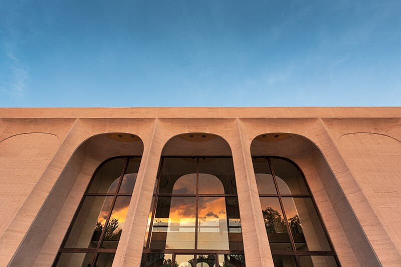 Low-angle photograph of the blue sky and the arches and lobby windows of the Sheldon Museum of Art lit by low-angle sun